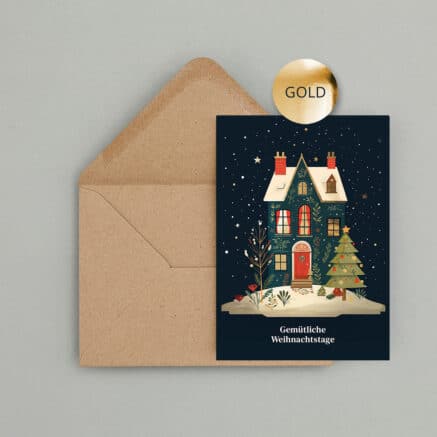 Weihnachtskarte mit verschneitem Haus, geschmücktem Weihnachtsbaum und dem Schriftzug „Gemütliche Weihnachtstage“. Goldene Veredelung setzt festliche Akzente auf dem dunkelblauen Motiv. Die Karte liegt vor einem braunen Kraftpapier Umschlag.